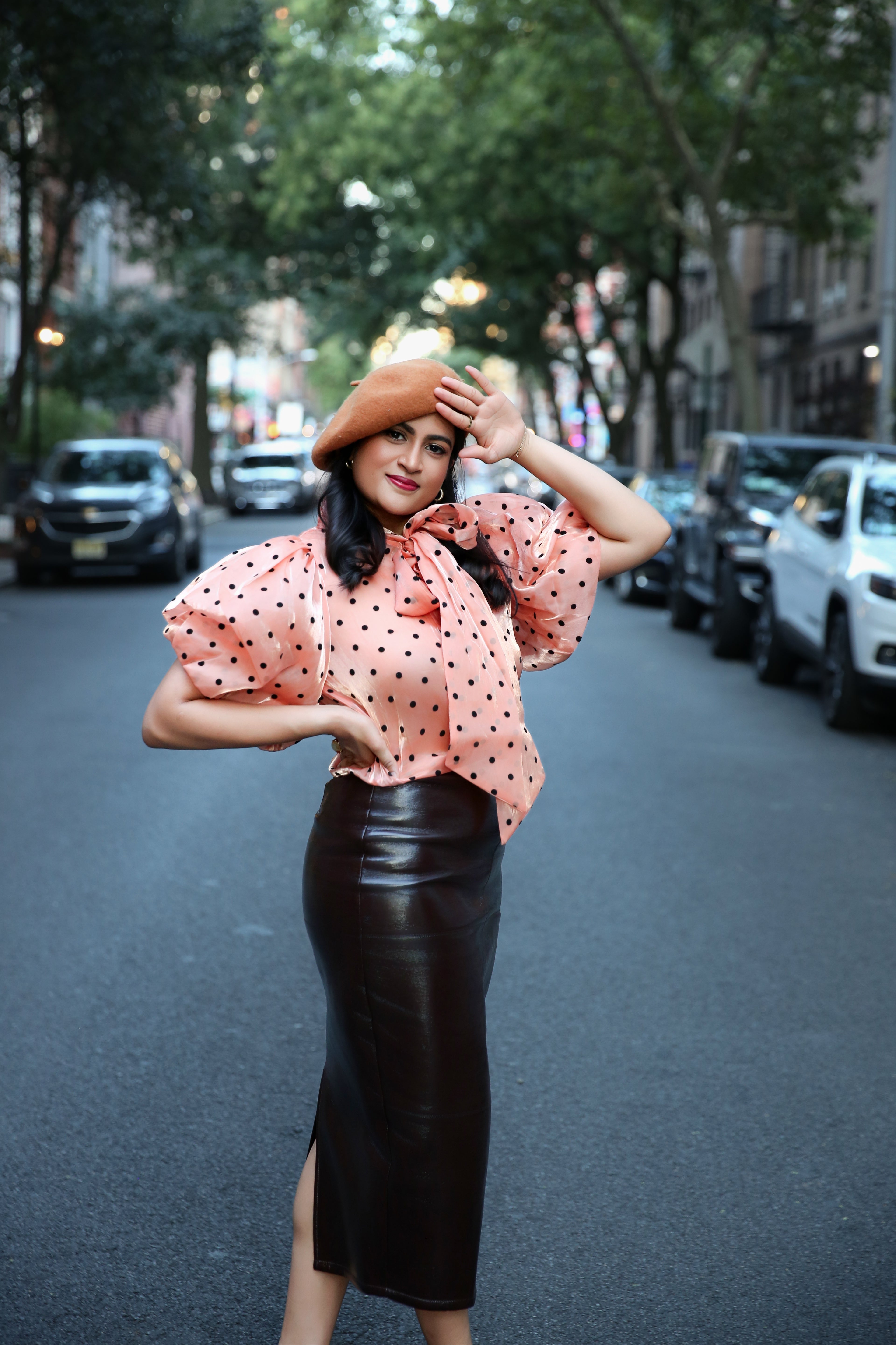 Woman in a pink blouse with polka dots and black leather skirt on a city street.
