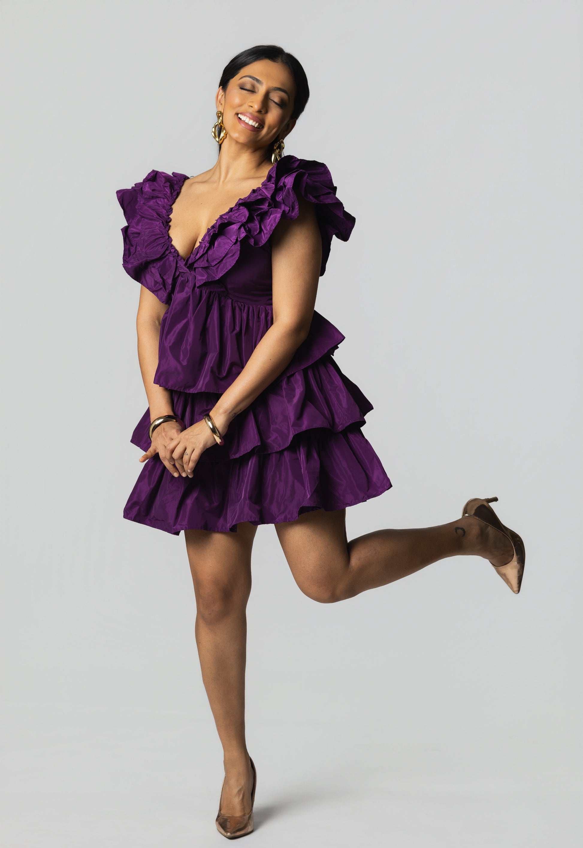 Woman wearing a purple dress posing against a gray background
