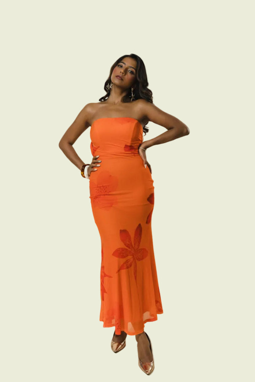 A woman modeling a strapless orange maxi dress with a tonal floral pattern, standing against a plain beige studio background.